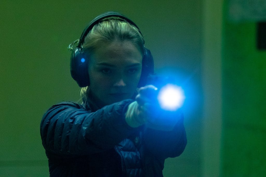 a pretty blonde lady shooting a gun in low light conditions
