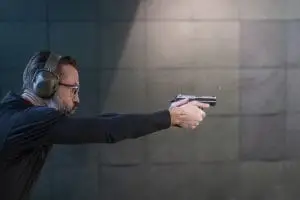 Shooter wearing eye and ear protection firing a handgun at an indoor shooting range