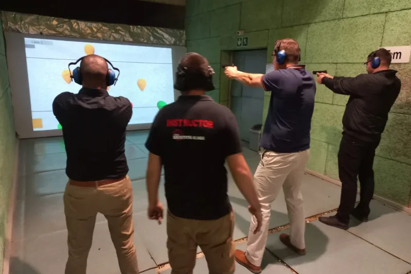 Firearm instructor supervising shooters using an interactive shooting simulator during a gun safety and marksmanship training session.